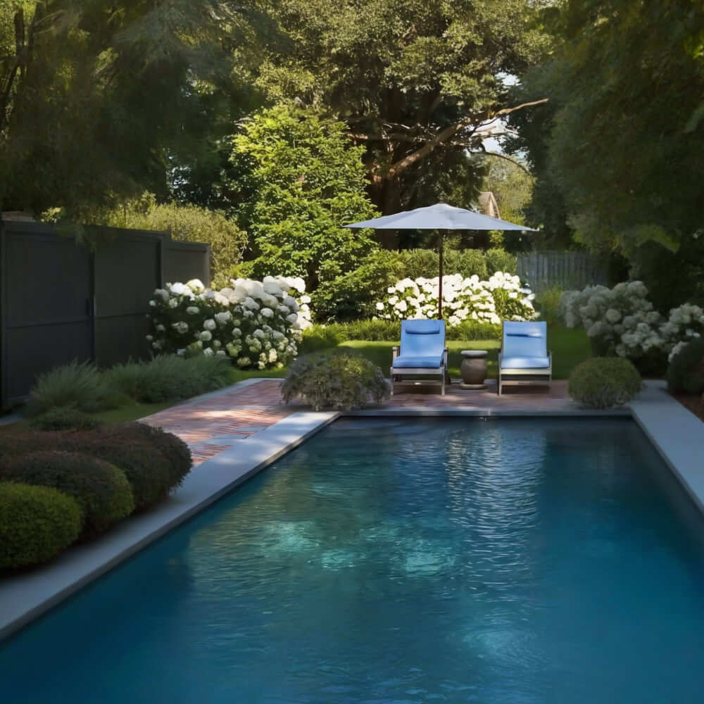 Our company designs outdoor areas around swimming pools, incorporating elements such as a stone patio with two sun loungers and a parasol. The area is surrounded by lush vegetation and white flowers, giving the garden a classic and calming aesthetic. We aim to create a harmonious environment that invites relaxation, while respecting the history and timeless character of the place.